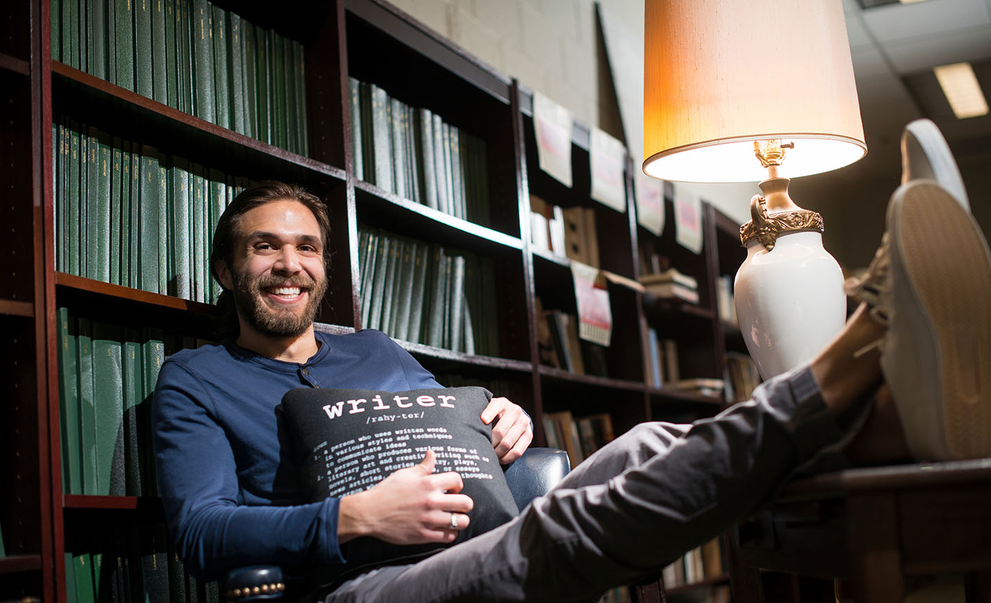 student in library holding  a pillow that says writer