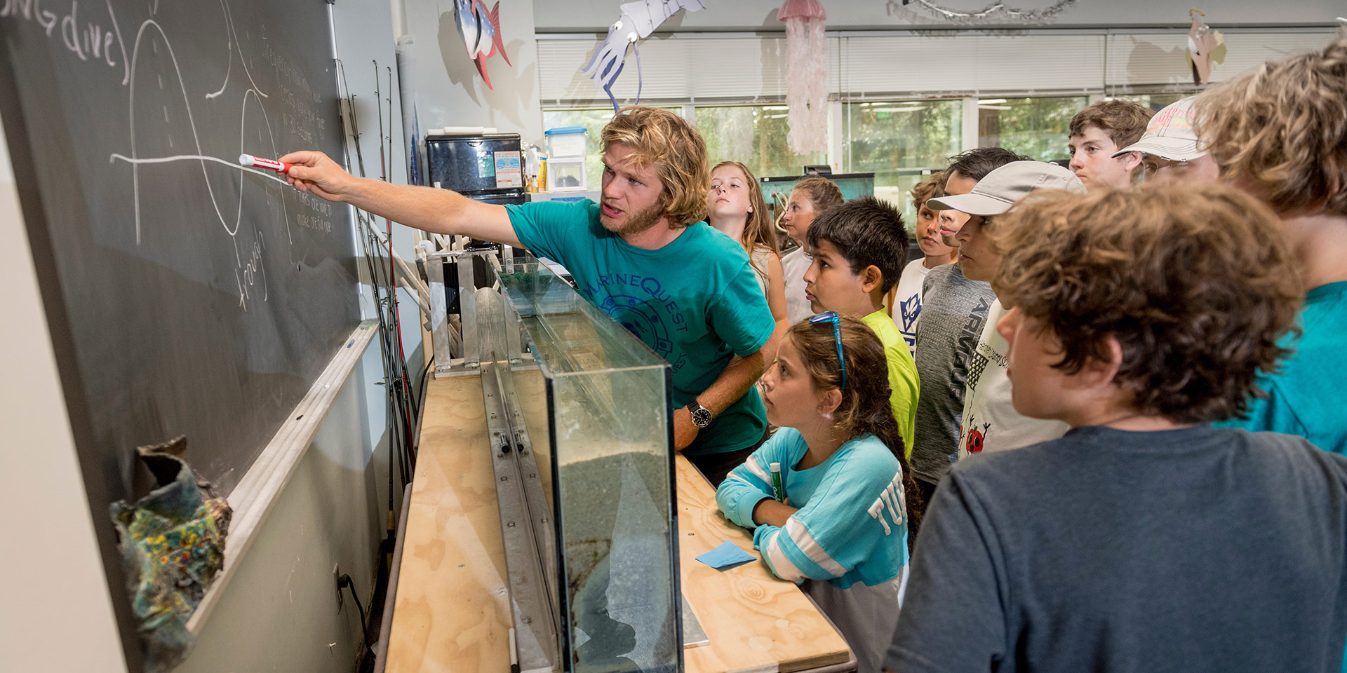 A student explains a diagram on a chalkboard to a group of students