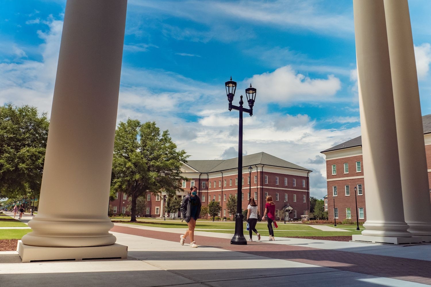 People cross the Health & Human Services Quad as seen between building columns 