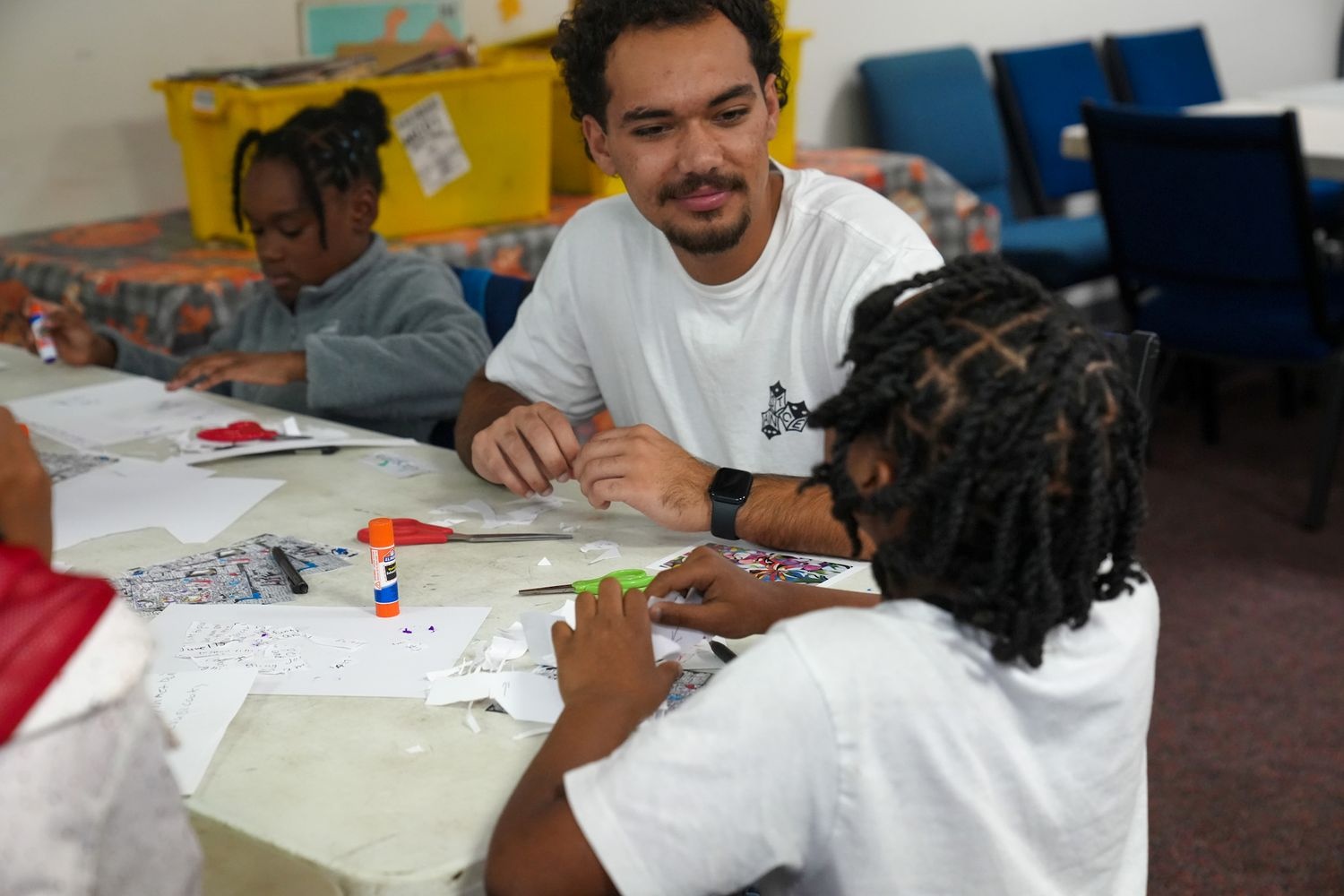 People sit around a table doing arts and crafts with paper, scissors, and glue sticks.