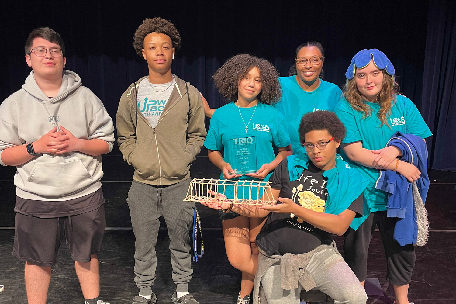 Students on a stage showing their bridge made out of popsicles for the bridge competition