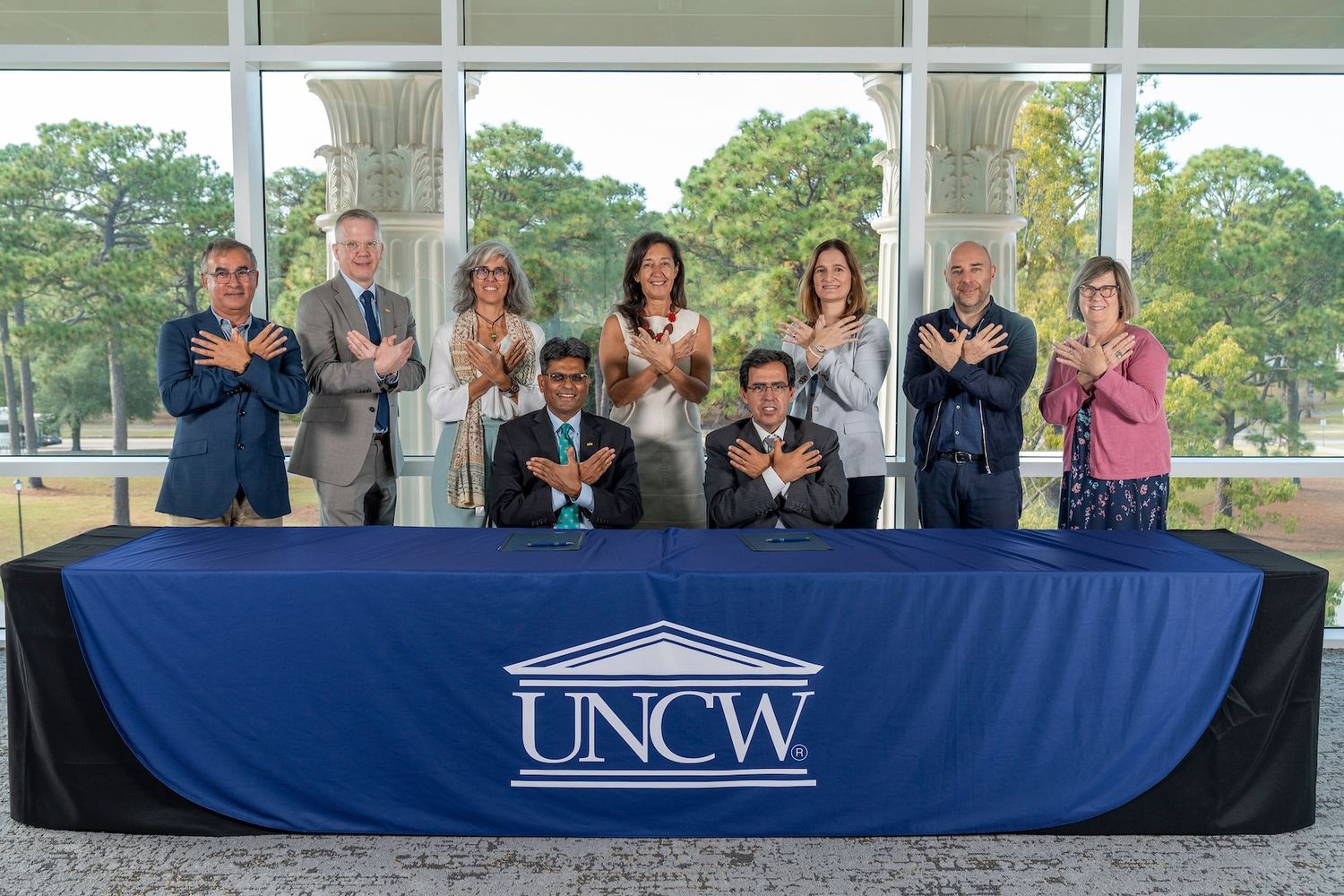 Chancellor Volety and other UNCW representatives with partners from algarve university display the "Wings Up" sign with their hands in the Lookout Lounge of Discovery Hall 