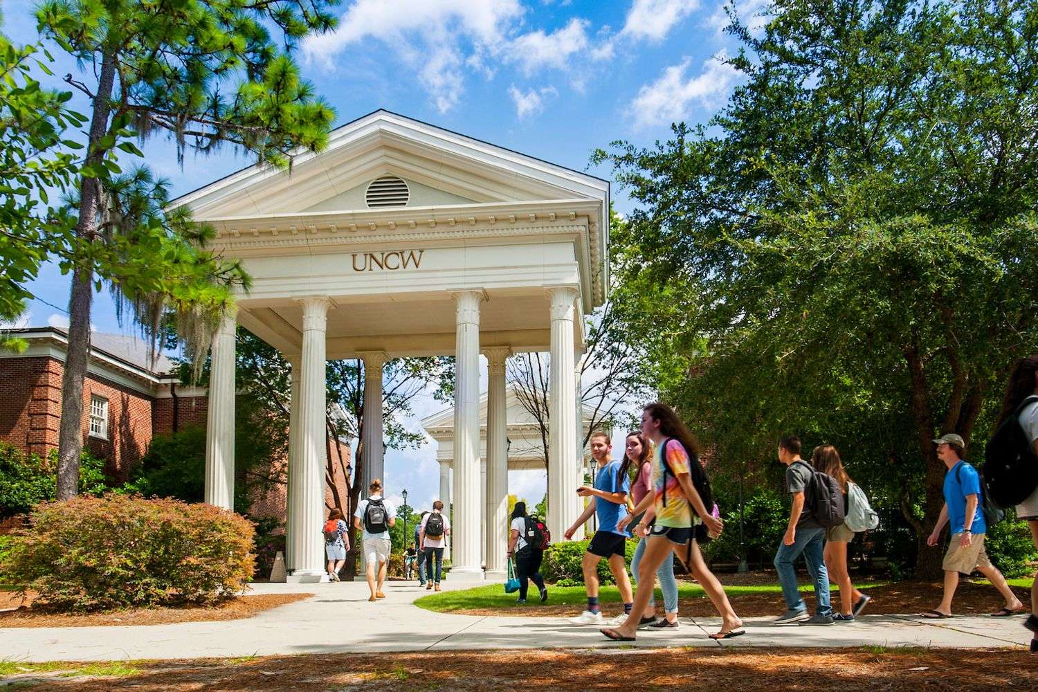Students walk on campus under the large scale UNCW archway and Georgian columns.