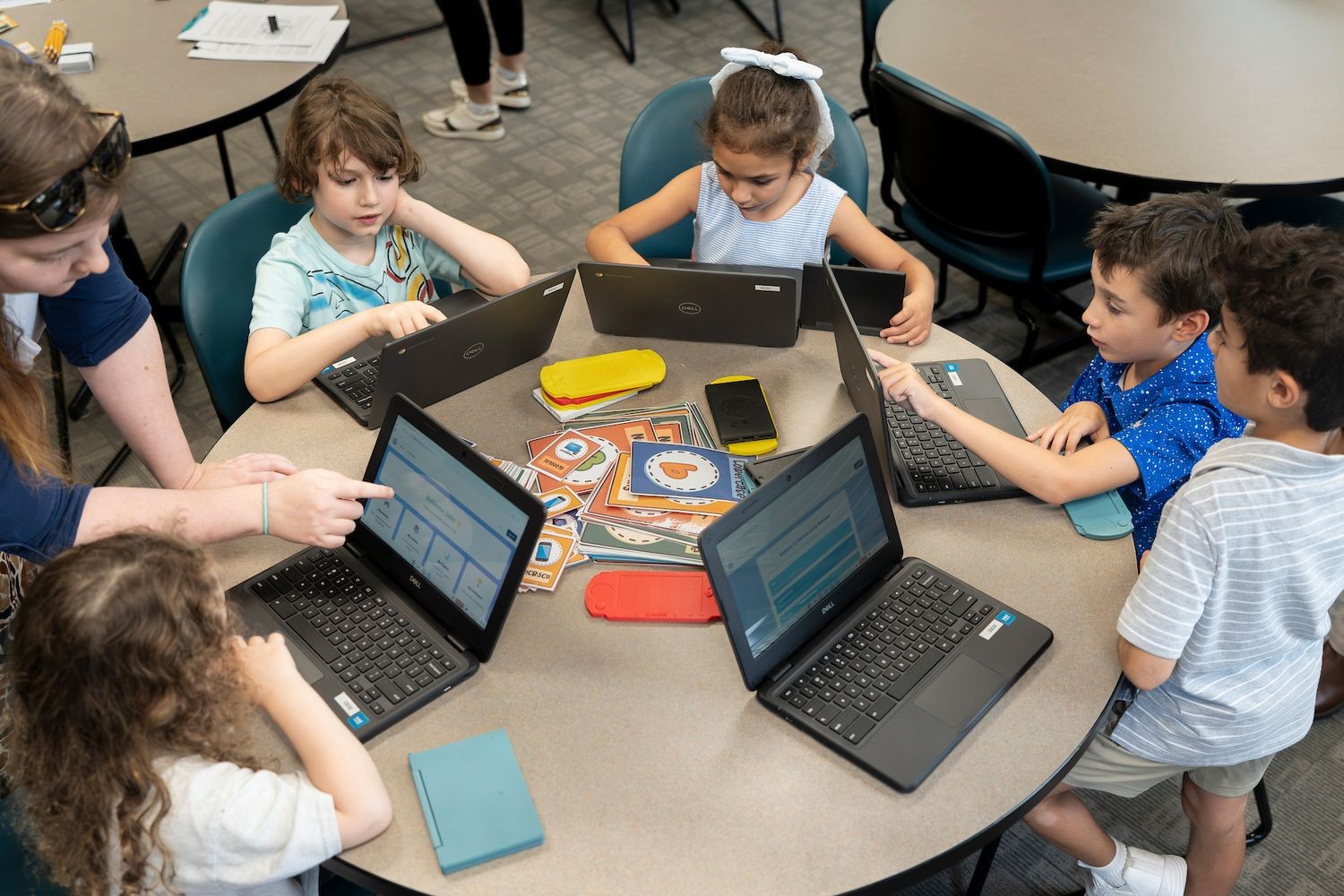 A group of kids sitting at a round table with a teach helping them